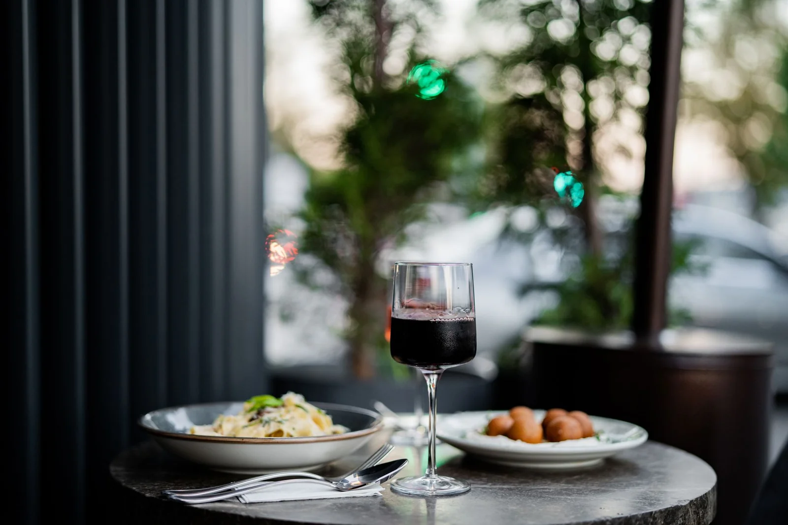 Verre de vin rouge et petite assiette posés sur un comptoir en bois dans un bar à vins